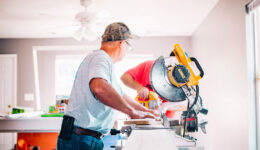 Older contractor cutting a wood board on a table saw for a home renovation.