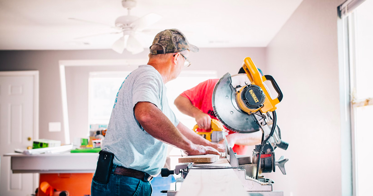 Older contractor cutting a wood board on a table saw for a home renovation.