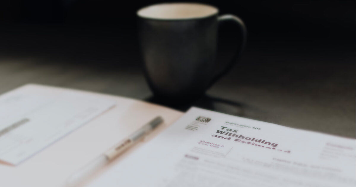 Blurry background of a black coffee cup and a file folder with tax withholding documents.